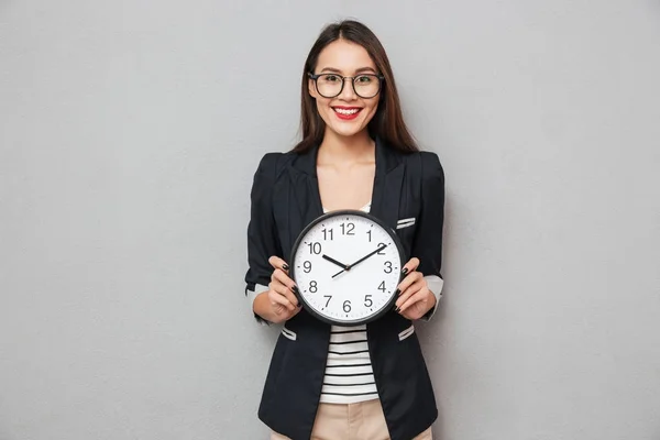 Mujer sonriente con anteojos sosteniendo el reloj y mirando a la cámara — Foto de Stock