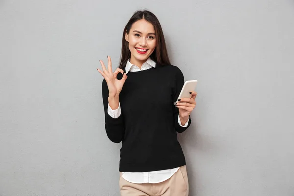 Tyytyväinen aasialainen nainen yritysvaatteissa tilalla älypuhelin — kuvapankkivalokuva