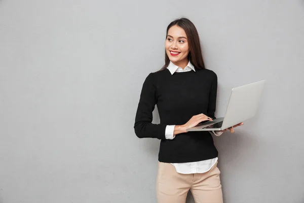 Pleased asian woman in business clothes holding laptop computer — Stock Photo, Image