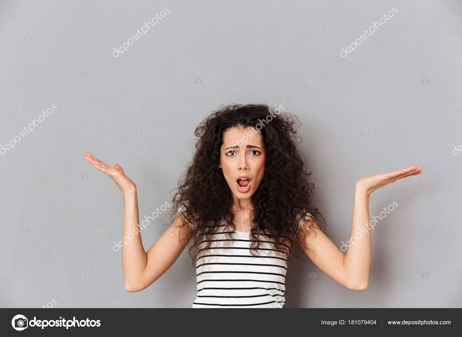 Pretty adult girl wearing striped tshirt throwing up hands mean