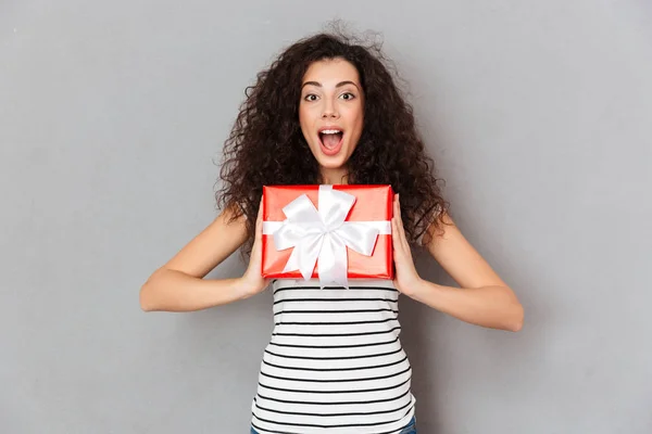 Agradável feminino 20s segurando caixa vermelha dom-embrulhado sendo animado um — Fotografia de Stock