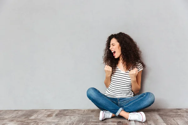 Jeune femme bouclée en vêtements décontractés exprimant plaisir tout en s'asseyant — Photo