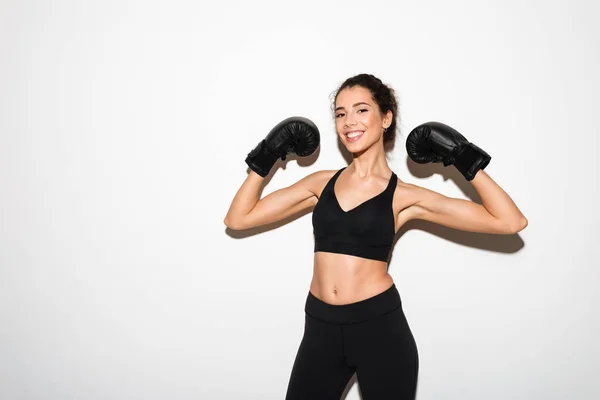 Lachende curly brunette fitness vrouw in bokshandschoenen tonen biceps — Stockfoto