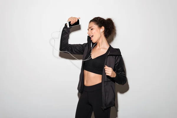 Playful curly brunette fitness woman listening music with closed eyes — Stock Photo, Image