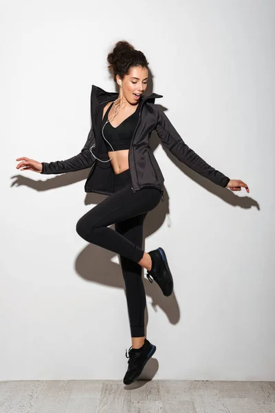 Fullängds bild av glada Lockig brunett fitness kvinna lyssnar musik — Stockfoto
