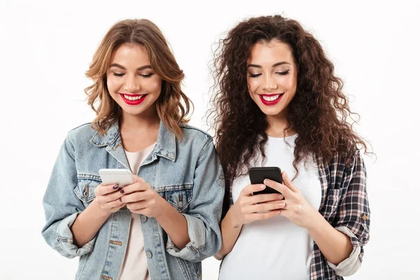 Imagen de dos chicas sonrientes escribiendo un mensaje en su teléfono inteligente — Foto de Stock