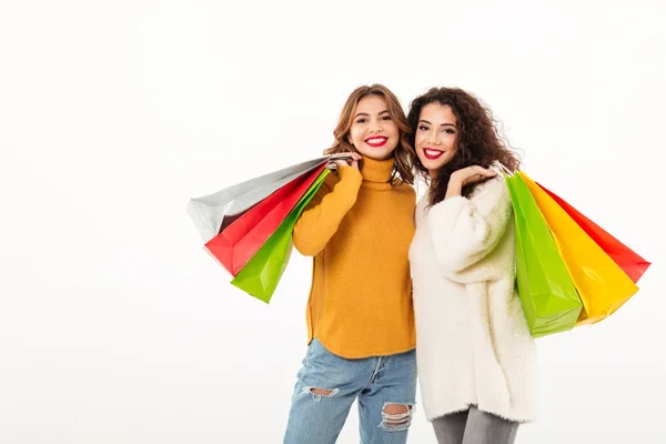 Две счастливые девушки в свитерах с пакетами, смотрящими в камеру — стоковое фото