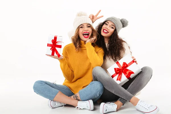 Twee gelukkige meisjes in truien en hoeden zitten met geschenken — Stockfoto