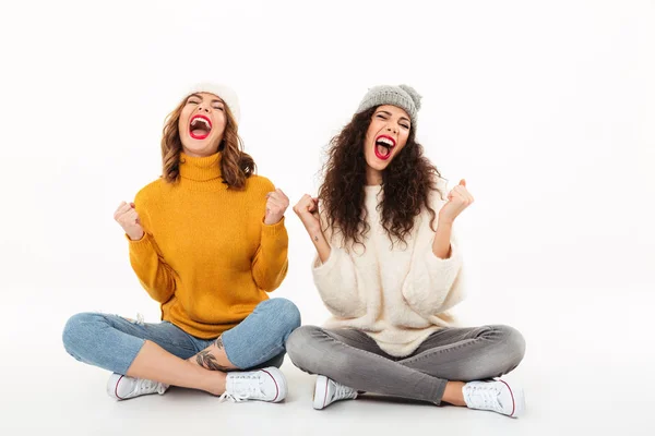 Due ragazze urlanti in maglioni e cappelli seduti sul pavimento — Foto Stock