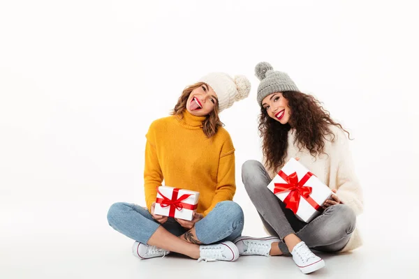 Twee speelse meisjes in truien en hoeden zitten met geschenken — Stockfoto