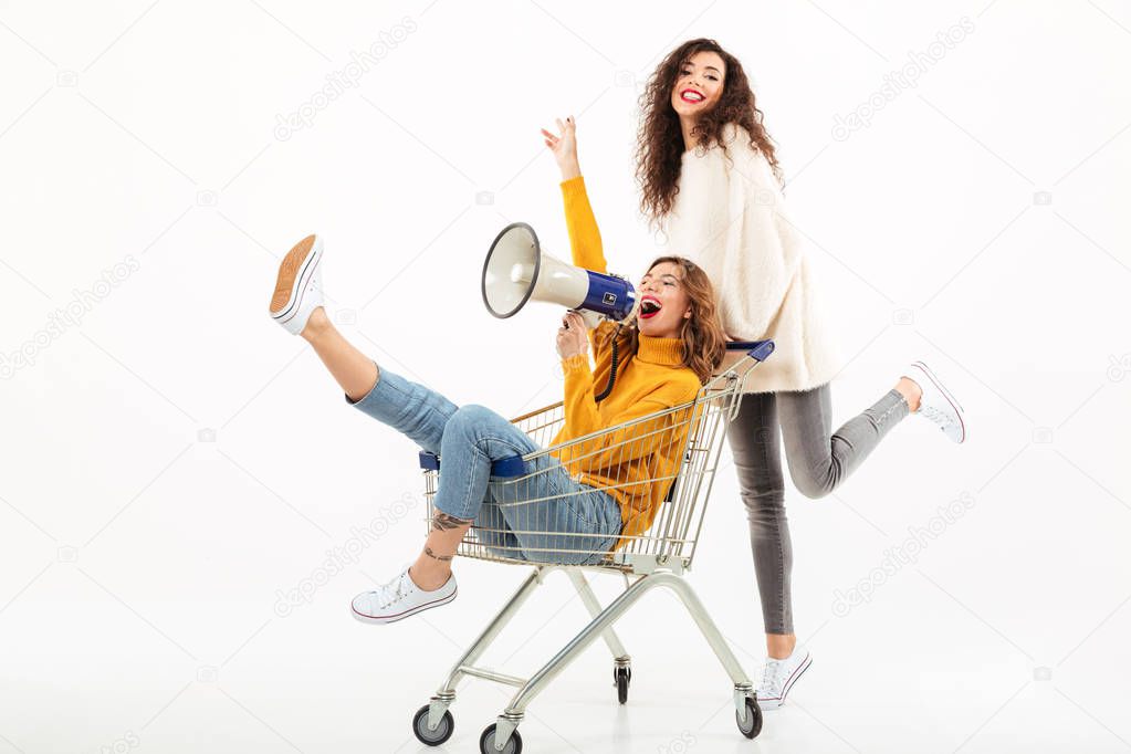 Two happy girls in sweaters having fun with shopping trolley