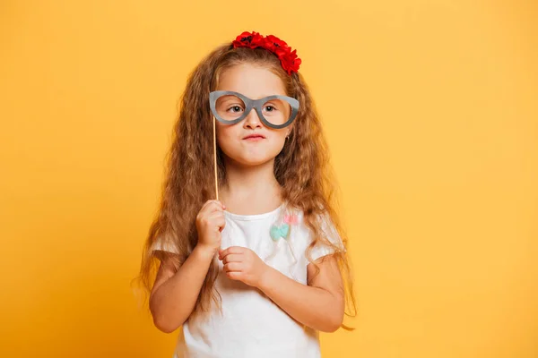 Graciosa niña sosteniendo gafas falsas mirando a un lado . — Foto de Stock