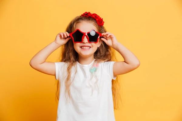 Pequeña linda chica sonriente con gafas de sol mirando cámara . — Foto de Stock