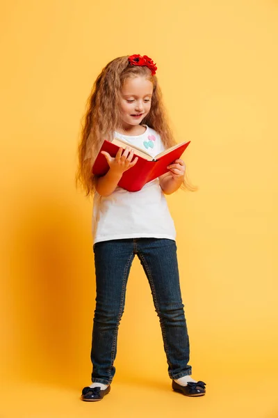 Konzentriertes kleines hübsches Mädchen liest Buch und schaut zur Seite. — Stockfoto
