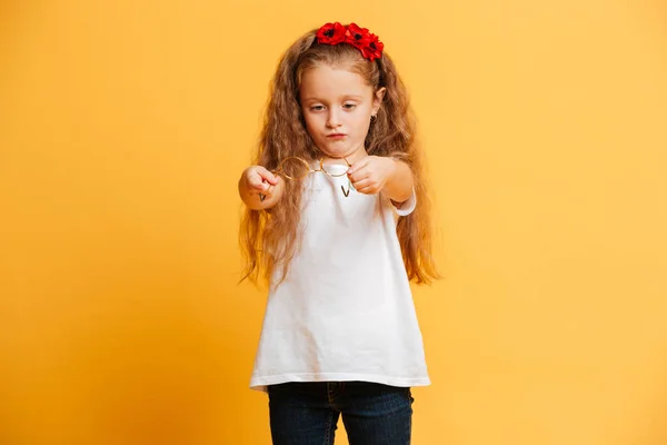 Weinig geconcentreerd mooi meisje bril op zoek opzij te houden. — Stockfoto