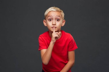 Gri arka plan üzerinde izole duran küçük çocuk çocuk resmi. Kamera sessizlik jest gösteren arıyorsunuz.