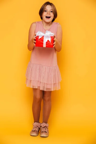 Happy surprised girl holding red present isolated over yellow