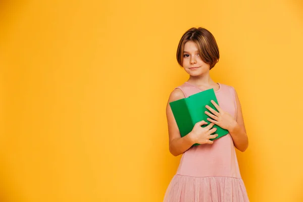 Mooi meisje in een roze jurk bedrijf groene boek geïsoleerd — Stockfoto