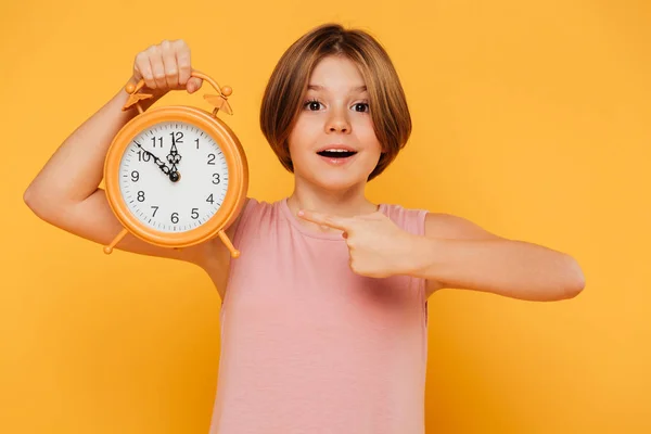 Happy girl pointing with finger at alarm clock isolated — Stock Photo, Image