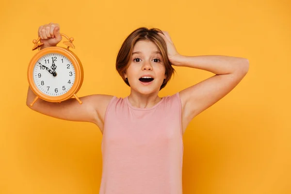 Surprised smiling girl showing alarm clock and holding her head isolated — Stock Photo, Image
