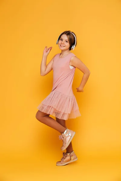 Chica sonriente divertida en auriculares bailando aislado sobre amarillo — Foto de Stock