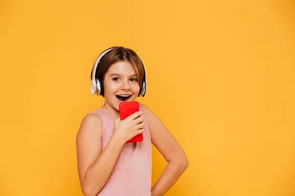 Chica feliz mirando a un lado, mientras que el uso de heeadphones y cantar en el teléfono inteligente aislado — Foto de Stock