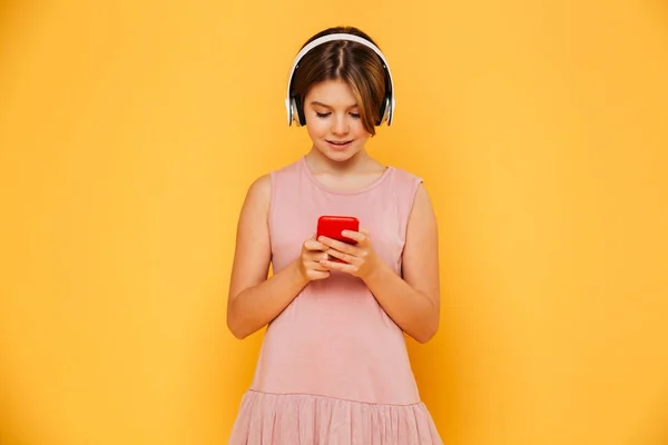 Chica sonriente ocupada usando teléfono inteligente y auriculares aislados — Foto de Stock