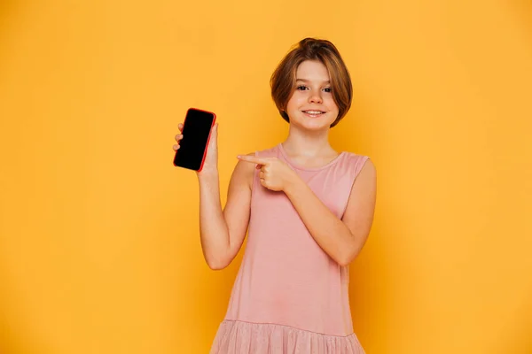 Chica sonriente apuntando a la pantalla en blanco del teléfono inteligente aislado —  Fotos de Stock