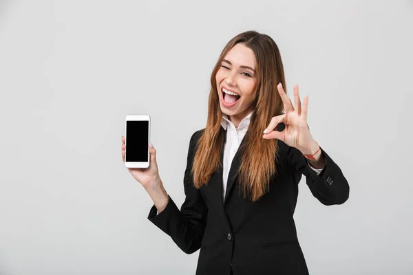 Senhora surpreso mostrando ok gesto e smartphone isolado — Fotografia de Stock