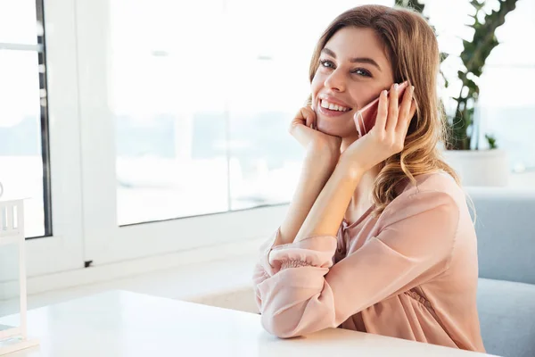 Smiling blondy woman in blouse sitting by the table