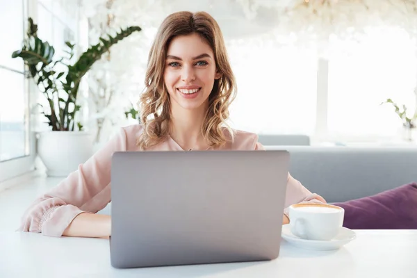 Mujer rubia sonriente en blusa sentada junto a la mesa — Foto de Stock