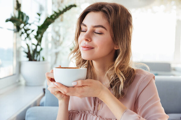 Portrait of gorgeous smiling lady smelling and drinking cappucci