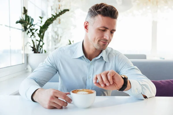 Portrait of handsome man sitting alone in city cafe with cup of — Stock Photo, Image