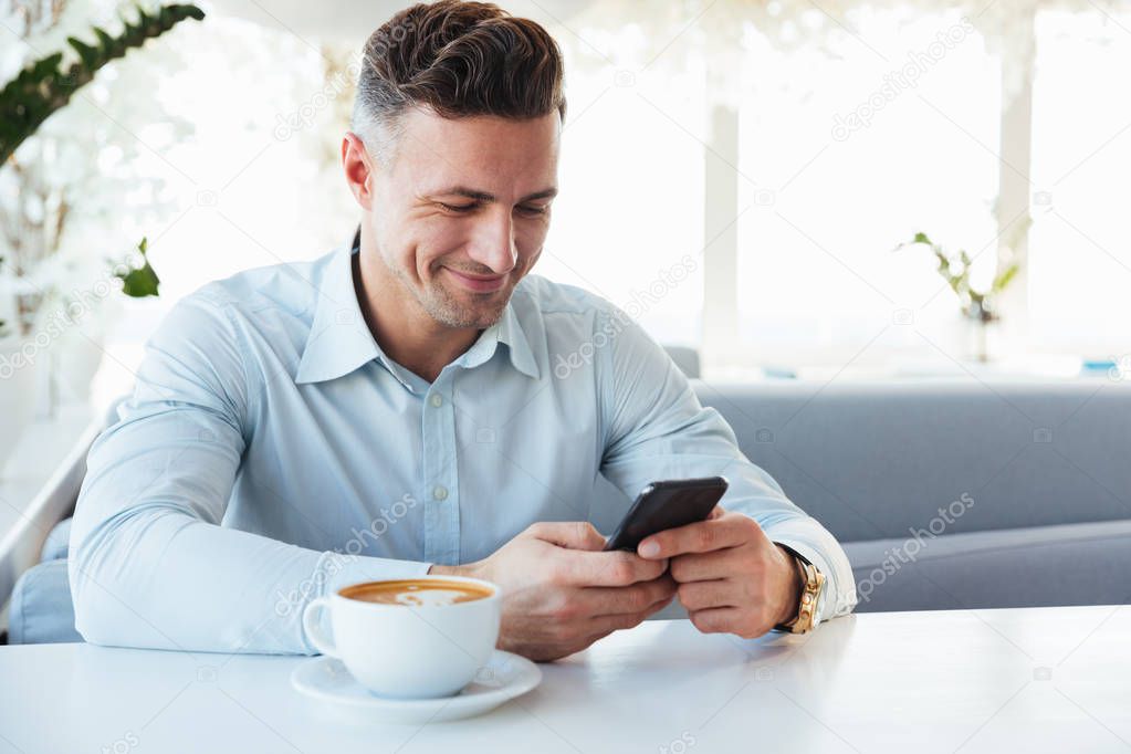 Image of joyful mature man sitting alone in city cafe with cup o