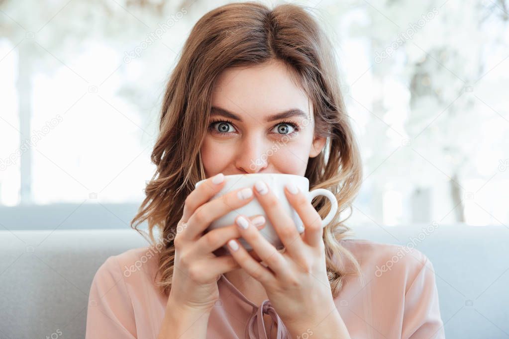 Portrait of a cheerful young woman holding cup of coffee