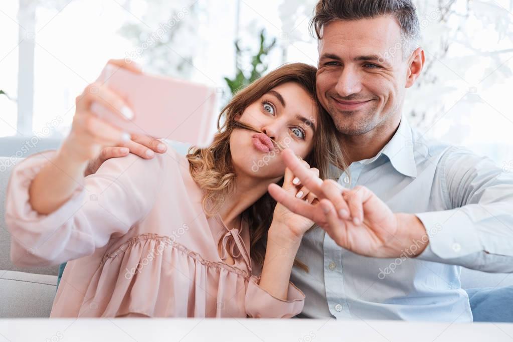 Photo of young and beautiful couple making selfie and fooling ar