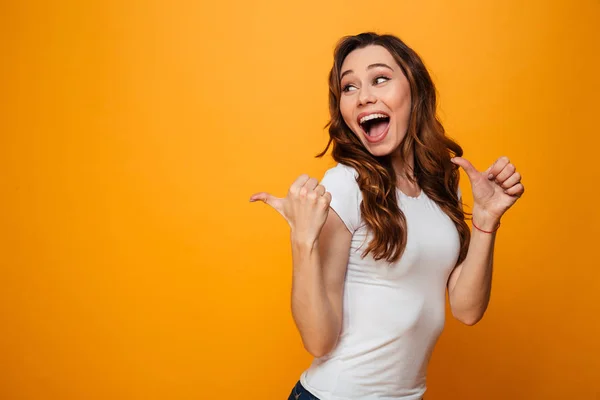 Glückliche brünette Frau im T-Shirt, die wegschaut und wegzeigt — Stockfoto