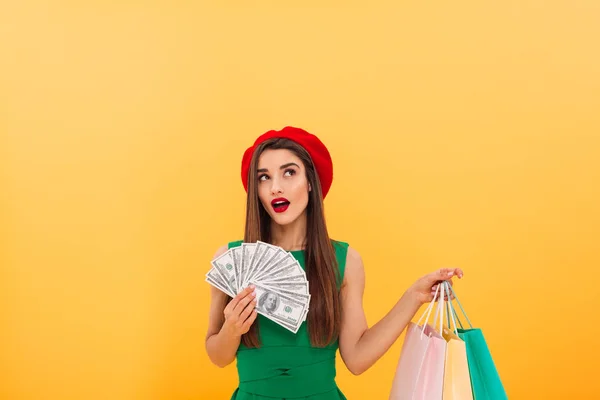 Pensando mujer joven sosteniendo el dinero y bolsas de compras — Foto de Stock