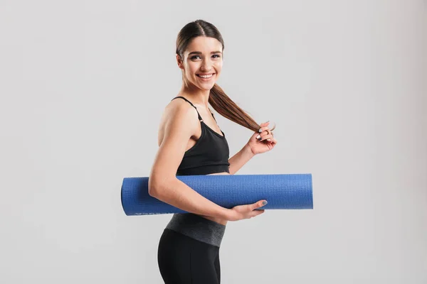 Foto van slanke jonge vrouw in trainingspak holding yoga mat en blik — Stockfoto