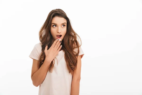 Verbaasd brunette vrouw in t-shirt die betrekking hebben op mond en weg op zoek — Stockfoto