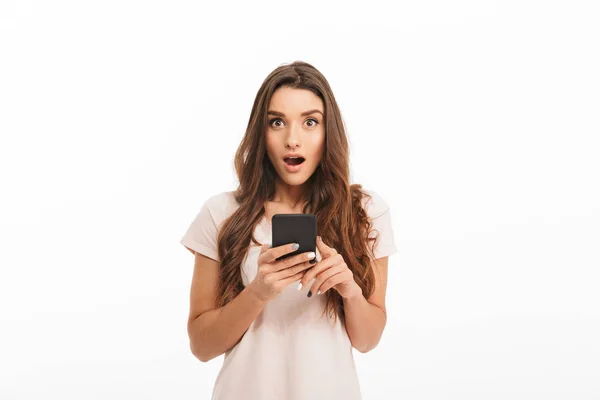 Překvapený brunetka žena v tričko hospodářství smartphone — Stock fotografie