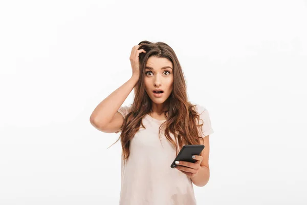 Geschokt brunette vrouw in t-shirt bedrijf smartphone — Stockfoto