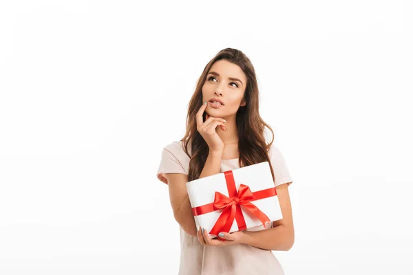 Fundersam brunett kvinna i t-shirt holding gåva och letar upp — Stockfoto