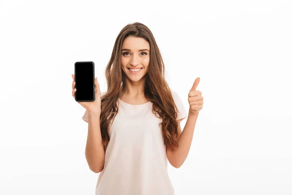 Happy brunette woman in t-shirt showing blank smartphone screen — Stock Photo, Image