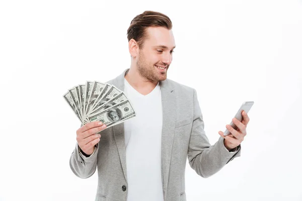 Joven empresario guapo alegre sosteniendo el dinero y usando el teléfono móvil . —  Fotos de Stock