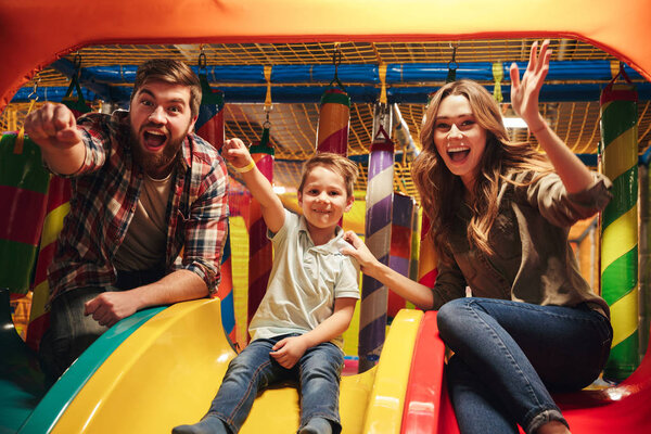 Веселый маленький мальчик, сидящий на слайде с родителями
