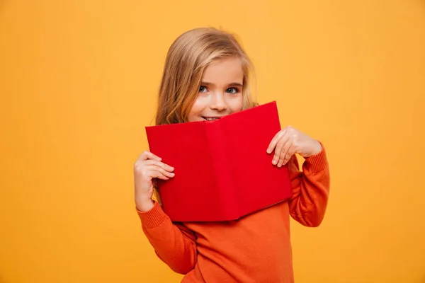 Улыбающаяся молодая девушка в свитере прячется за книгой — стоковое фото