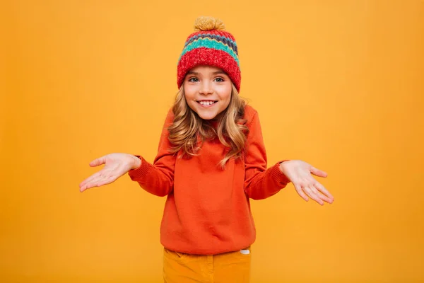 Usměvavá mladá dívka v svetr a čepice krčí rameny — Stock fotografie