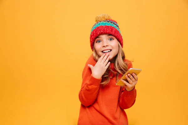 Zmatená dívka v svetr a čepice držení smartphone — Stock fotografie