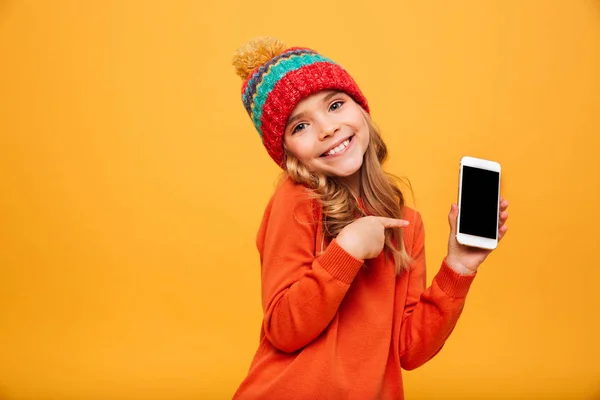 Chica agradable en suéter y sombrero que muestra la pantalla del teléfono inteligente en blanco —  Fotos de Stock